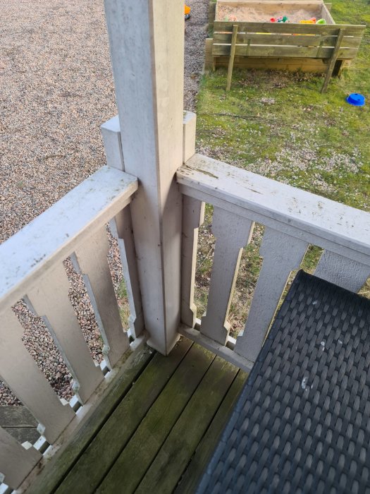 Sliten entrétrappa med ett vitmålat räcke, en stolpe syns nära kameran, tecken på förfall synliga.