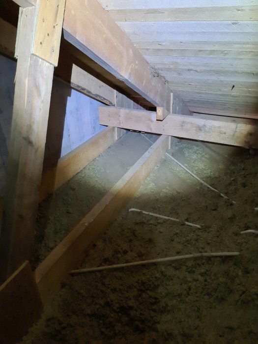 Takstol och vinkeljärn syns i en vindsmiljö, vilka indikerar strukturella komponenter i ett husbygge.