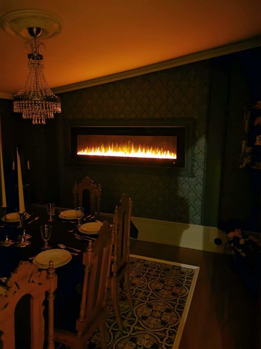 Stämningsfull matsal med tänd modern öppen spis, kristallkrona och dukat bord med mörka toner.