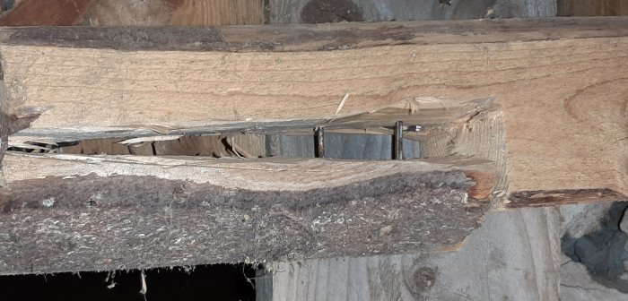 Delad träbalk i krypgrund med spikar och 3-4 cm glipa som behöver reparation.