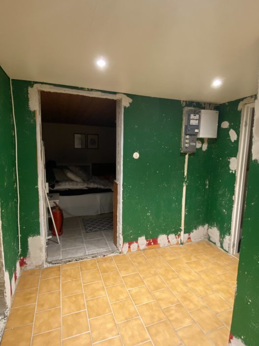 Renoverad vägg med spacklade ojämnheter och synliga utrymmen efter borttagna trösklar, gult kakelgolv.