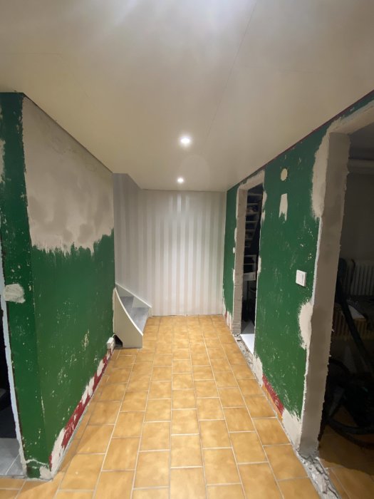 Renoverad korridor med nyligen spacklade väggar och synliga tröskelområden redo för jämnning.