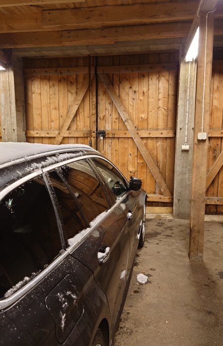 En delvis täckt bil framför gamla trägarageportar av 50x200-brädor som är murkna nertill.