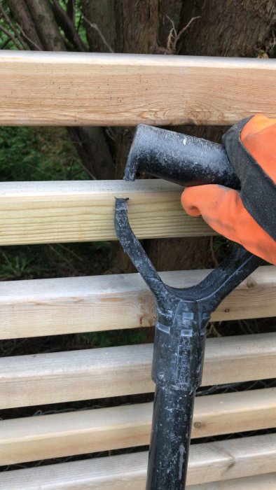 En hand i orange handske håller en skyffel använt som stöd för arbete.