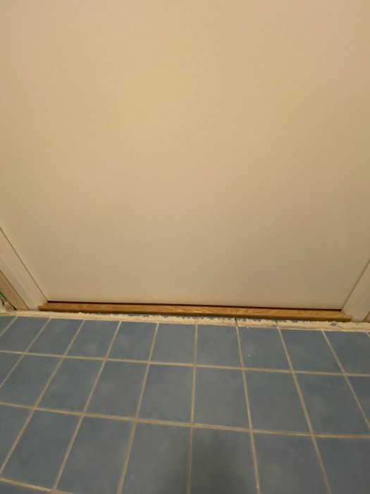 Nyinstallerad badrumsdörr med synlig glipa mellan karm och kakelgolv, behov av foder eller tätning.