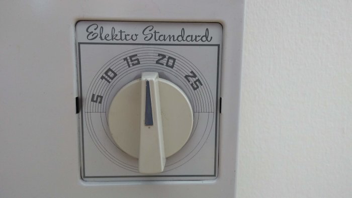 Gammal termostat märkt "Elektro Standard" med en inställningsratt för temperatur på en vit vägg.