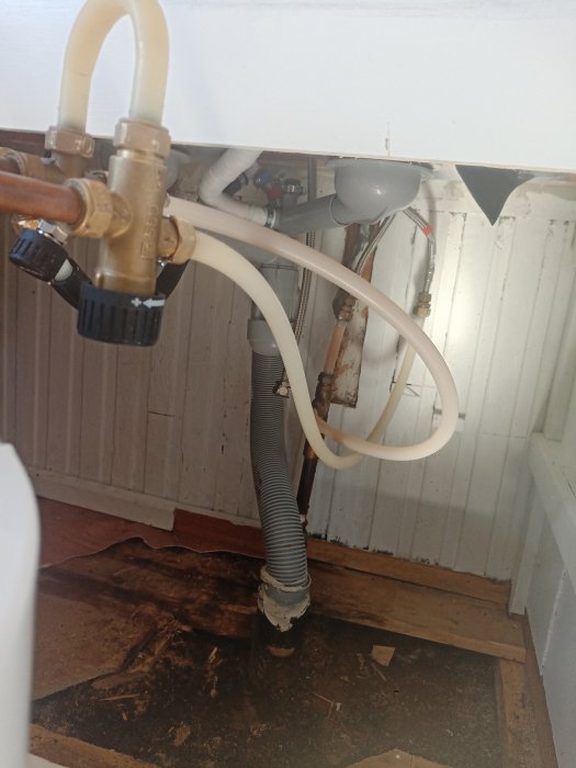 Köksrörinstallation under diskbänk med synliga vattenledningar och avloppsslang.