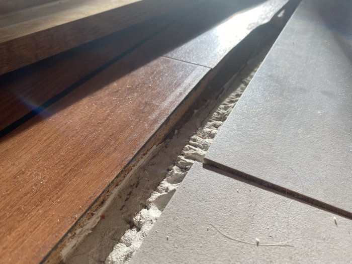 Ojämna golvplankor med synlig dålig utförande vid ett hemmabyggprojekt i soligt rum.