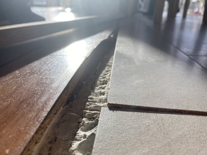 Ojämn övergång mellan trägolv och klinkergolv med synlig spackel och glipa.