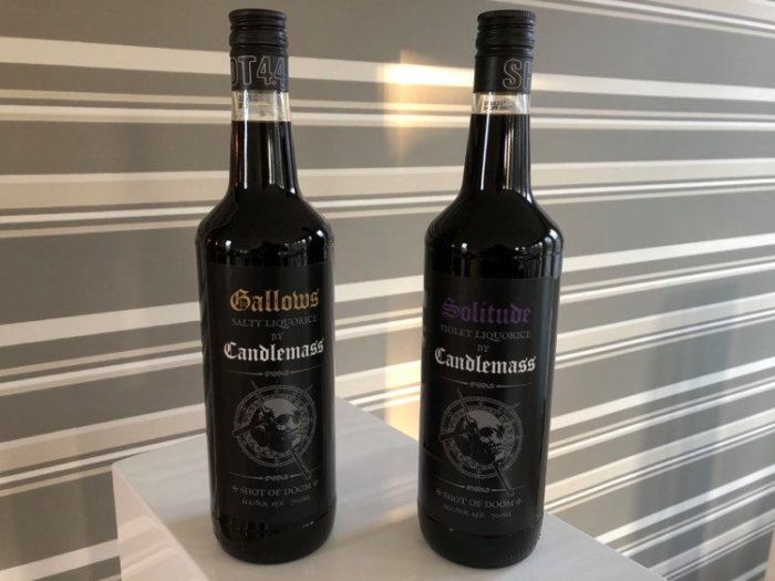 Två flaskor lakritslikör märkta "Gallows" och "Solitude" från Candlemass på ett randigt bord.