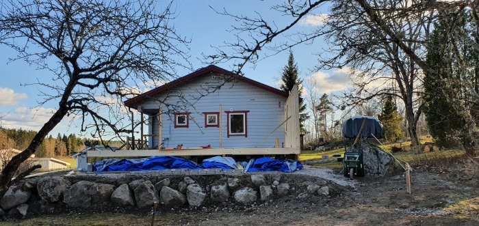 Nyuppförd trävägg på en husgrund med existerande hus i bakgrunden och byggmaterial i förgrunden.