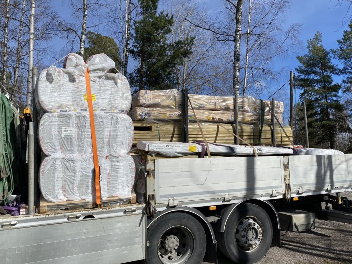 Lastbil fullastad med byggmaterial såsom isolering och träbrädor, redo för byggprojekt.