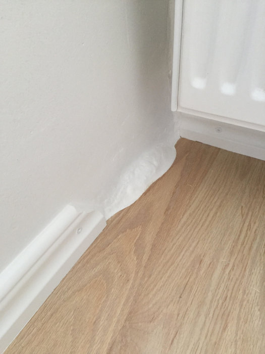 Fogning mellan golv och vägg intill vit panel, nytillämpad vit fogmassa.