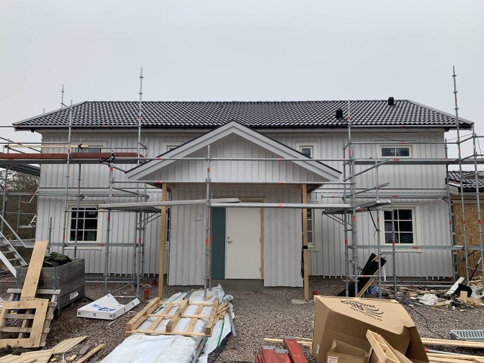 En nybyggd husfasad med panel och läkt, omgiven av byggnadsställningar.