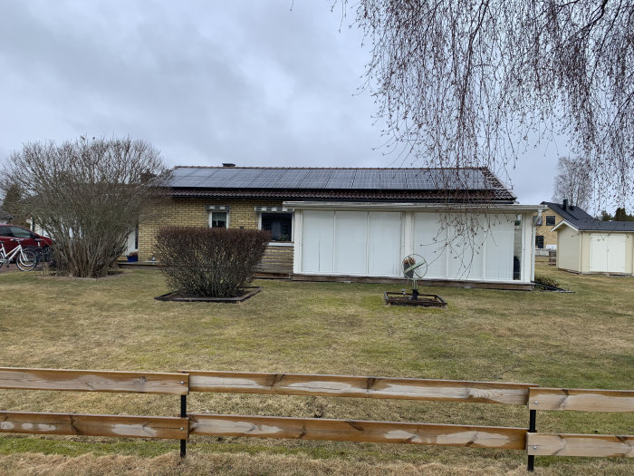 Enplanshus med solpaneler på taket och en delvis synlig bil och cykel till vänster.