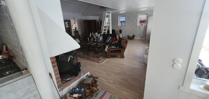 Vardagsrum under renovering med braskamin, trägolv och oplacerade möbler.
