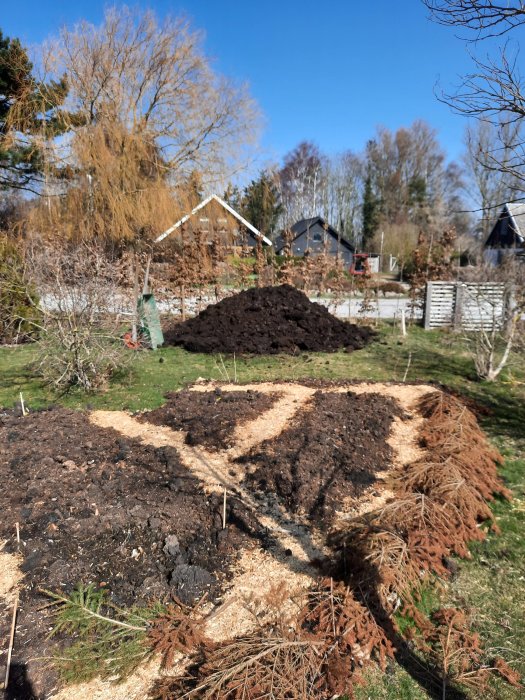 Hög med brunnen hästgödsel i en trädgård använd för gödning, med hus och träd i bakgrunden.