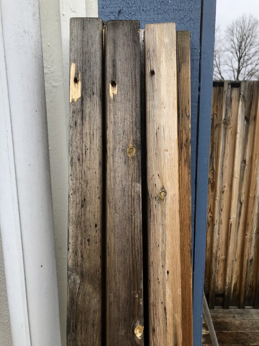 Missfärgade och fläckiga tryckimpregnerade träspjälor på ett staket som behöver underhåll.