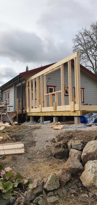 Byggkonstruktion av träväggar på en husgrund med existerande hus i bakgrunden.