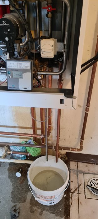 Värmesystem Danfoss ECL110 med tömda rör och hink full av vatten under öppen ventil.