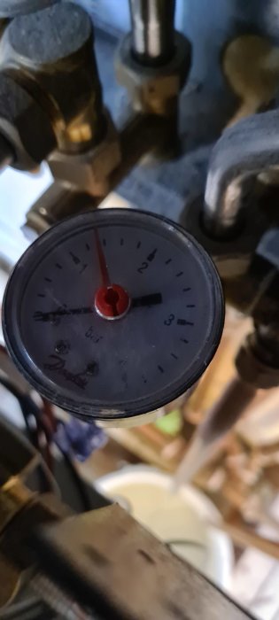 Manometer med röd visare på 1.5 bar mot oskarp bakgrund, visar tryck i värmesystem.