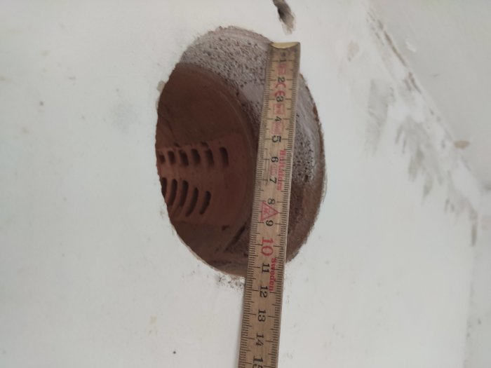 Mätning av ventilationshål i en vägg med en tumstock, 11.5 cm i diameter, redo för igensättning.