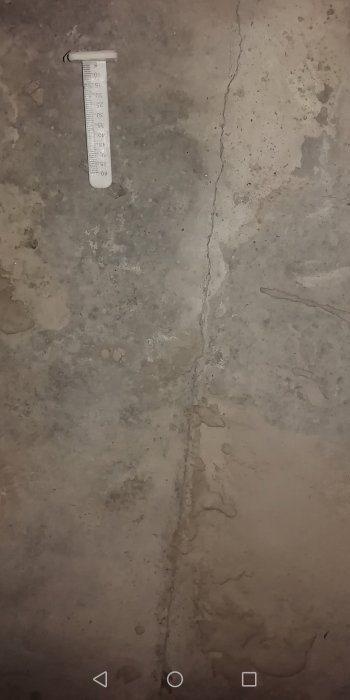 Sprickor på ett nyligen gjutet grått källargolv med en termometer som indikerar temperaturen.