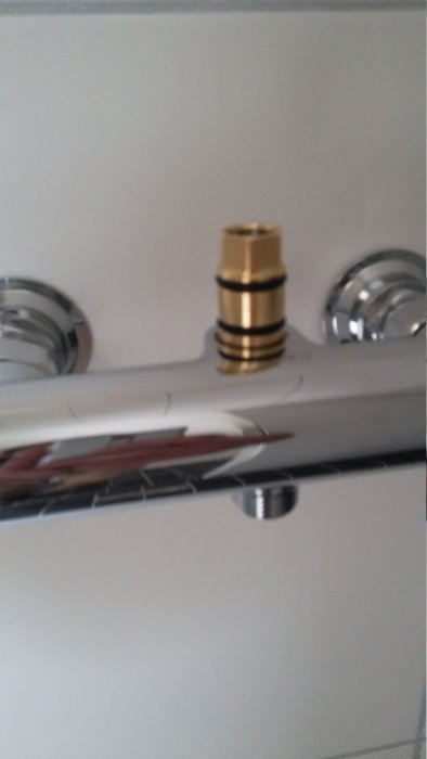 Närbild på en duschblandare med en ovanlig guldfärgad koppling som inte är en skruvkoppling.