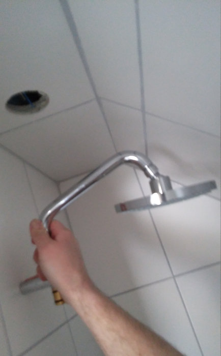 Person som håller i en kromad duschstång framför en snedvägg i ett badrum under renovering.