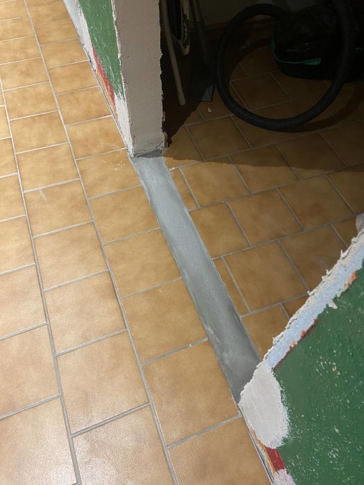 Nygjutet betongtröskel mellan tegelgolv och en grön dörrkarm, visar avlägsnande av tidigare trösklar.