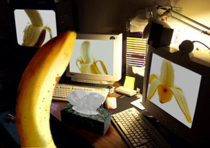 Banan framför skärmar med bilder på skalade bananer som ser ut som ben, skrivbordsmiljö.