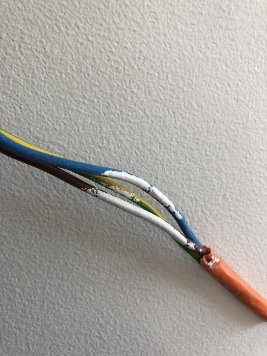 Elkabel med färgstänk från slarvig målning på en vitmålad vägg.