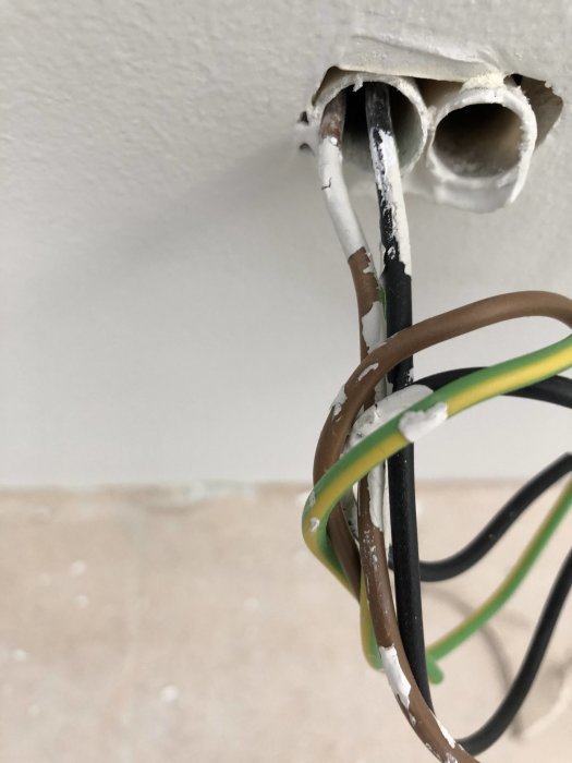 Eluttag och kablar med bortslarvad vit färg på en vägg vid renovering.