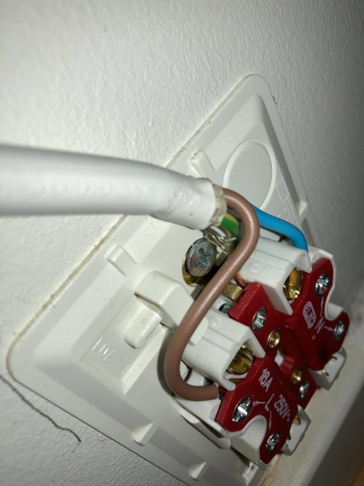 Närbild av ett öppet eluttag med synliga anslutningar och en kabel som går in.