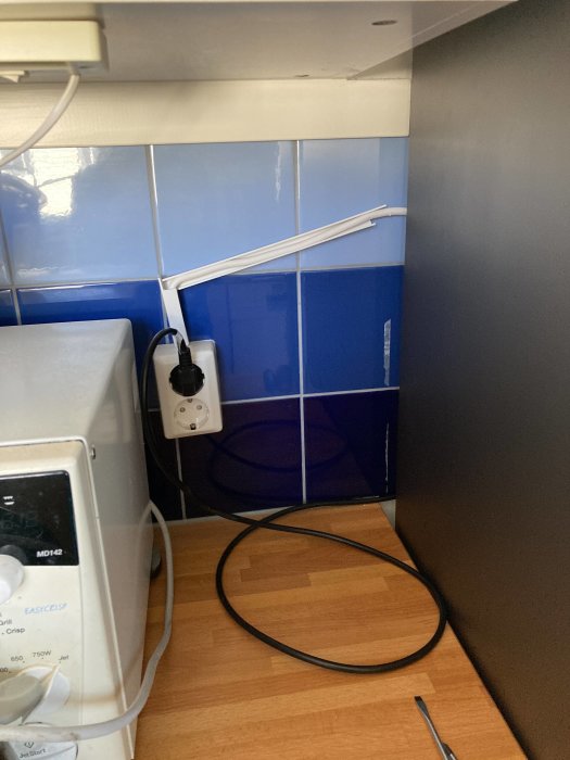 Eluttag med inkopplad vit sladd ovanför bänkskiva och lös svart kabel på golv i kök.