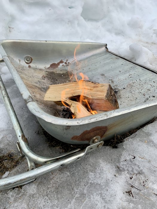 Brinnande vedbitar i en gammal vagnkärra omgiven av snö.