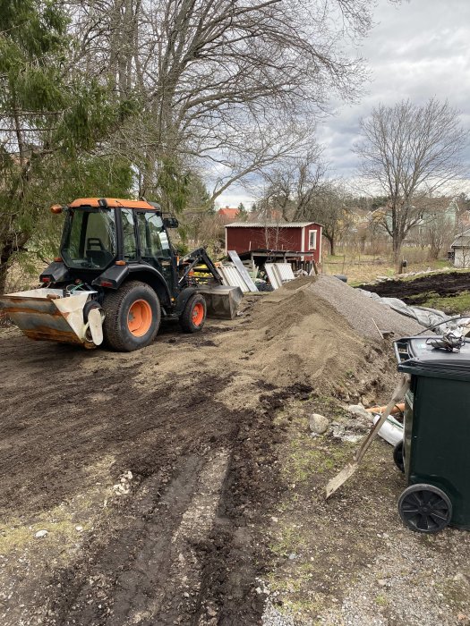 Traktor och sandhög på lerig mark med verktyg och material vid byggprojekt för pool.