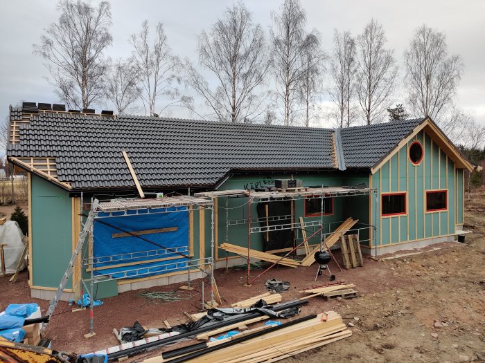 Hus under renovering med nytt taktegel nästan färdiglagt och byggmaterial framför huset.