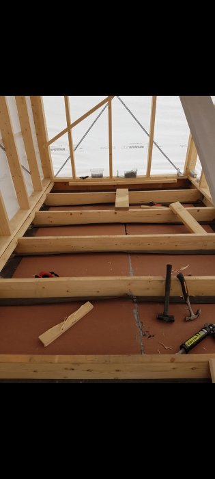 Installation av montageband under vindpappen i en takstolskonstruktion med verktyg och byggmaterial.