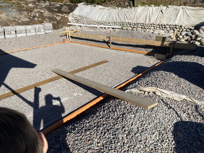 Gjutform av träreglar för betongsula på makadamunderlag med mätverktyg, i ett soligt utgrävningsområde.