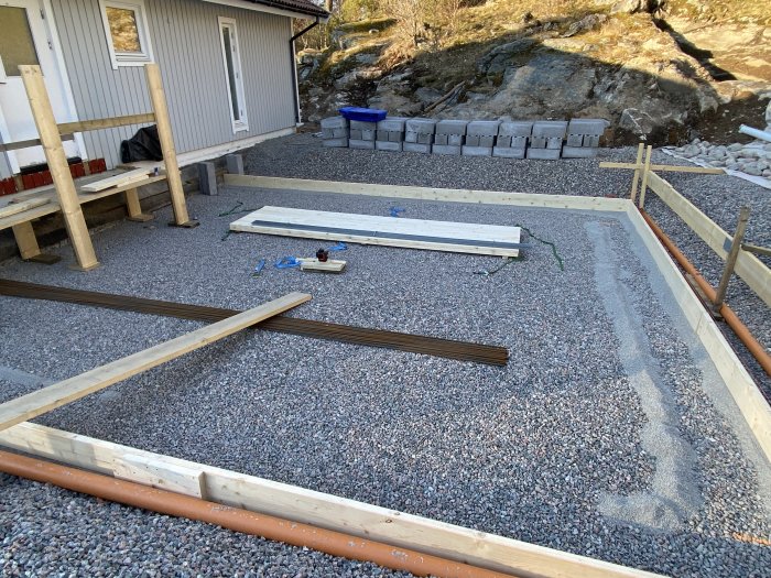 Utgrävning för utbyggnad med grus, reglar till gjutform för betong, och befintligt hus i bakgrunden.