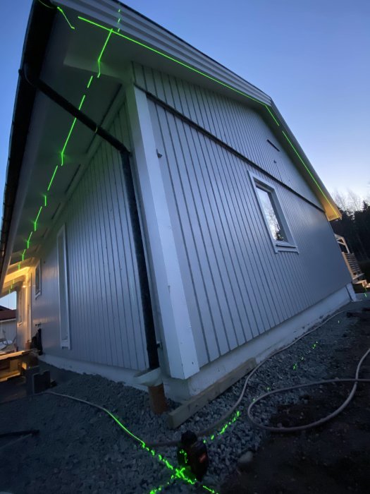 Utgrävning för nybyggnation med synliga gröna lasermärken för nivåkontroll vid husgrund i skymningen.