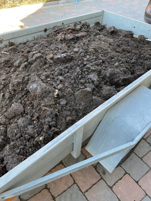 Släpvagn fylld med brunnen hästgödsel på en inritad uppfart.