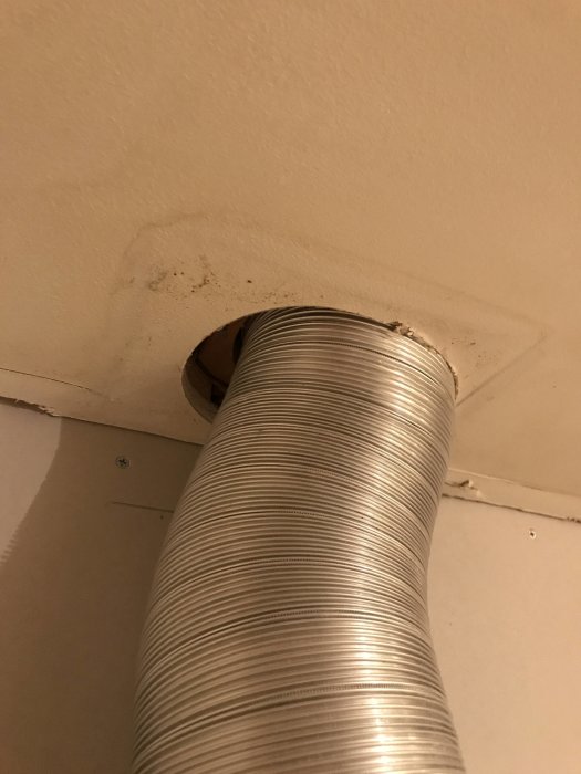 Aluminium flexrör som sträcker sig genom ett ofullständigt hål i taket, omgivet av spackel och en synlig träkant.
