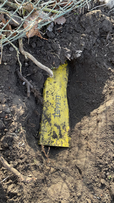 En gul varningsskylt för en fiberkabel som är delvis grävd i jorden vid en tomtgräns.
