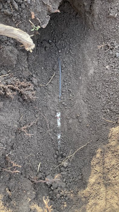 Ett uppgivet grävt hål i jorden visar en exponerad kabel som löper genom marken, täckt av en liten skylt ovanpå.