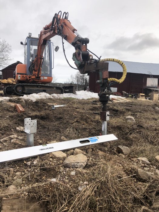 Grävmaskin som installerar jordankare i marken med vattenpass framför på ojämn terräng.