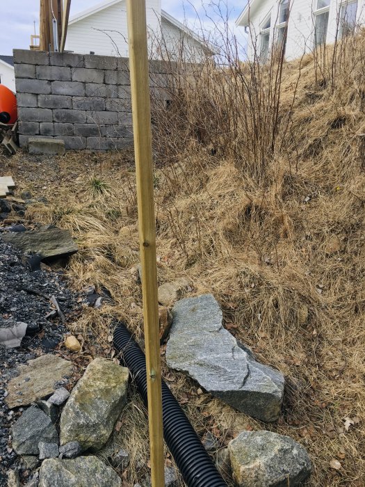 Brant slänt med sprängsten, småsten och torrt gräs vid ett hus, svårtillgänglig för bygge av altan.