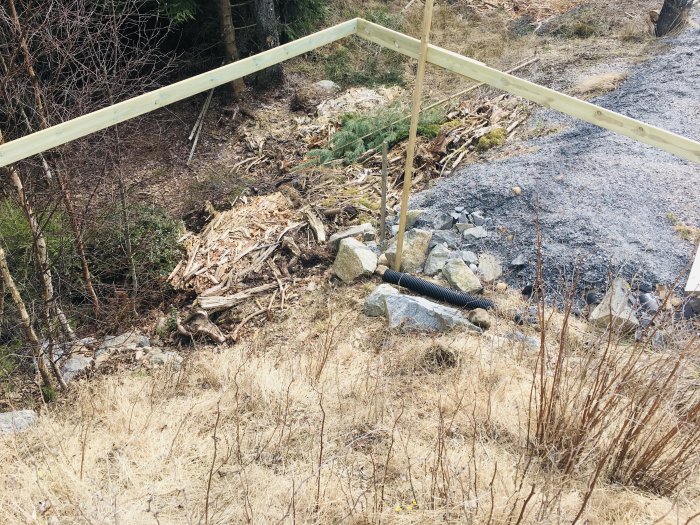 Brant slänt med sprängsten och vegetation, synligt regelverk för altanbygge i förgrunden.
