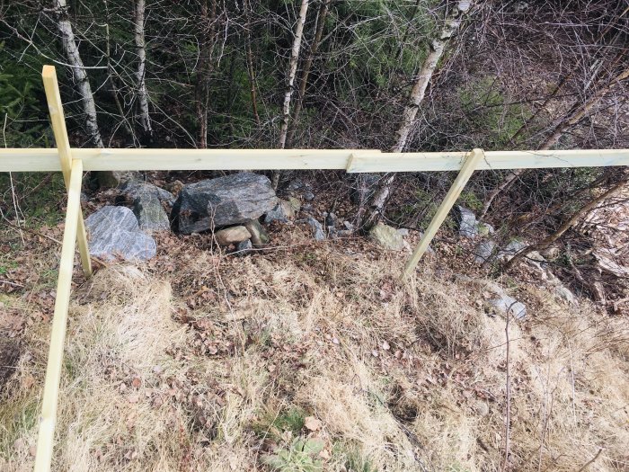 En början på ett träregeleverk för altanbygge på en slänt med sprängsten, småsten och vegetation.